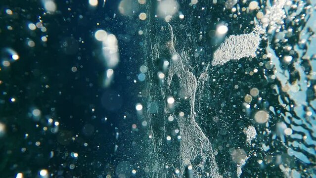 Air bubbles under seething surface of waves at sunset, underwater shot