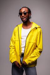 Trendy young african american man in sunglasses grimacing while wearing windbreaker jacket isolated on grey