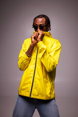 Young african american man in sunglasses wearing bright yellow windbreaker jacket isolated on grey © Dmytro Hai