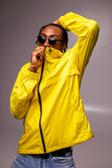 Stylish african american man with braids wearing sunglasses and bright windbreaker jacket on grey background