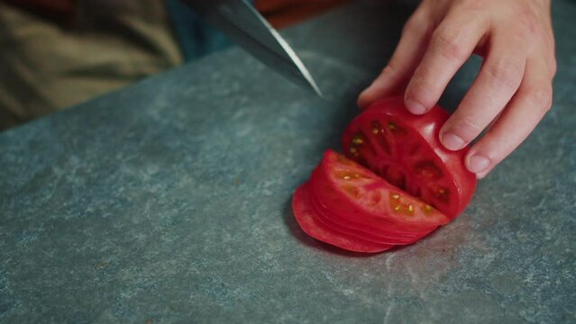 The cook uses a sharp knife to cut the tomatoes into thin slices