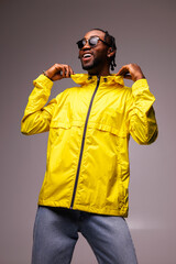 Smiling young african american man in sunglasses posing in yellow windbreaker jacket isolated on grey © Dmytro Hai