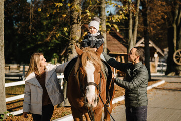 Happy father, mother, son caress horse outdoors. Kid riding a horse. Family having fun spring...