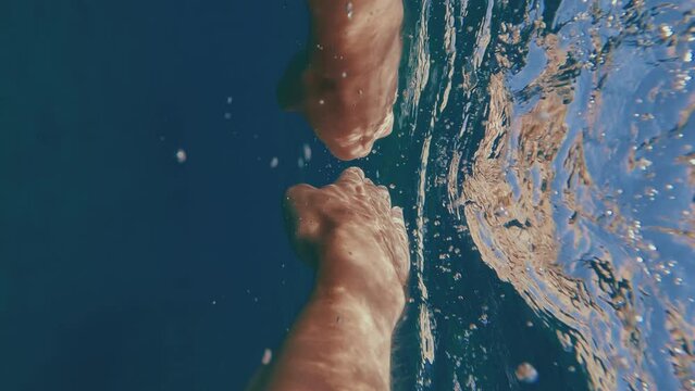 POV shot, split level, guy paddling with his hands underwater to rocky shore