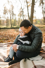 Dad embraces son child sitting on blanket on golden leaves in park. Father hugging kid have picnic in autumn forest in nature. Family holiday, spending time together at sunset. Autumn mood. Closeup.