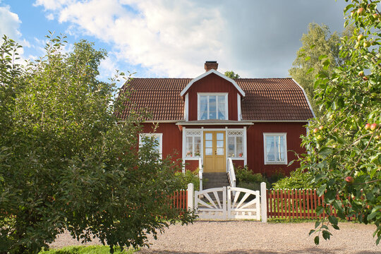 a typical red and white swedish house in smalland. White garden gate, brown fence