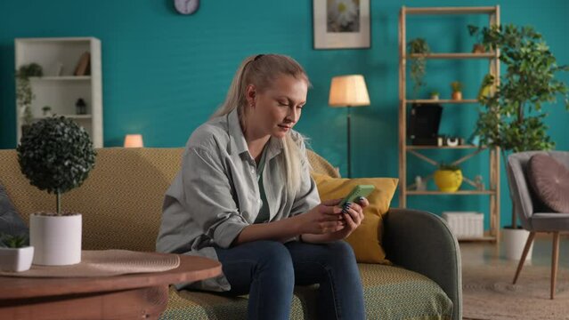 A woman using a smartphone while sitting on the sofa at home close up. A woman looks through social networks, photos, videos. The woman smiles and is sad, indulging in memories.