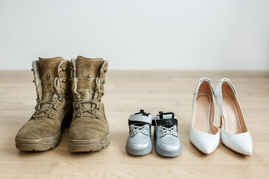 Old worn military boots, women's shoes and baby shoes on wooden floor. Veteran and family concept.