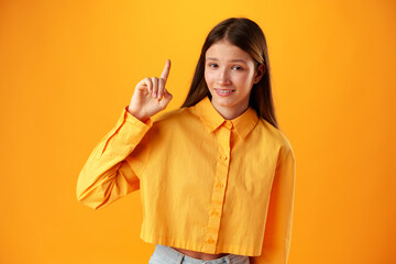 Teenager girl over yellow background pointing finger to copy space