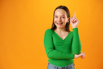 Teenager girl over yellow background pointing finger to copy space