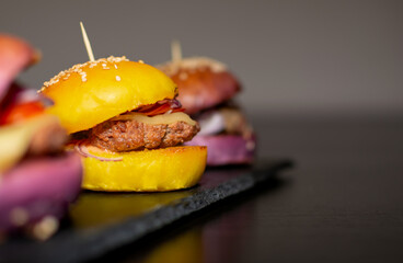 Colored Mini Gourmet Burgers with sesame seeds on black slate board