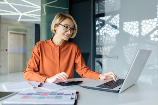 Young female financier with calculator working inside office at workplace, businesswoman behind paper work satisfied smiling, good achievement results, working with contract, accounts and charts.