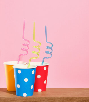 Bright blue, yellow and red festive paper cups with different drinks stand with colored straws on a wooden surface. Copy space for text.