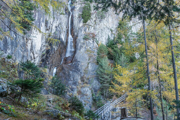 Obraz premium Wooden footpath and waterfall on a rocky mountain in a forest on an autumn day.