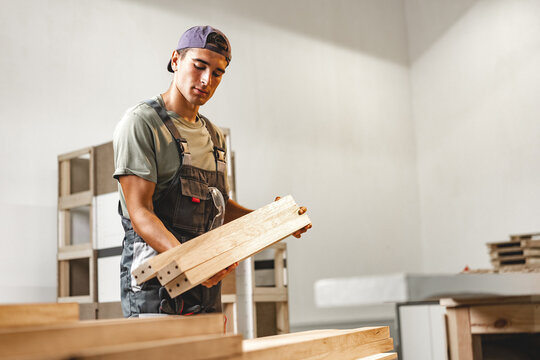 Young carpenter man looking and choosing wood plank at workshop in carpenter wood factory