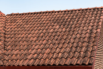 Red terracotta ceramic tiles on the roof over the brick wall of a residential building. Diagonal pattern, wavy shape. Traces of dampness and black mold