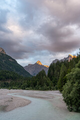 The setting sun hitting the peak of the mountain above a glacial, blue river in the alps in Slovenia