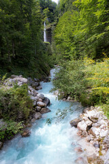 A turquoise river running down through the forest from a large waterfall in Slovenia