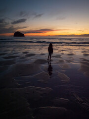 Silhouette of a girl standing on a beach at low tide as the sun sets in the background in Cornwall, UK