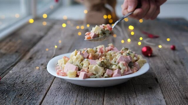 Homemade New Year is Olivier salad on a wooden background. A man's hand puts a traditional Russian Christmas salad with a spoon.