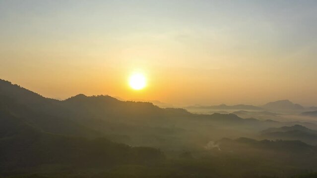 Aerial hyperlapse The sun gradually sets over the mountain..The sky is painted with streaks of yellow and orange..The fading light casts a gentle glow on the fog.
