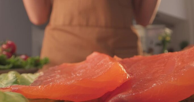 Making sandwich with lettuce and salmon. Female chef puts salmon slices to prepare tasty morning sandwich at home. Extra close-up shot