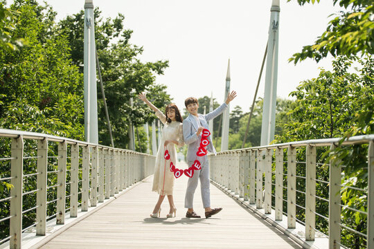  A young male and female couple are enjoying themselves while taking wedding pictures on the bridge with a placard.