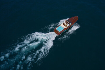 Luxury wooden big speedboat fast moving on dark water top view. Expensive wooden big boat with people moving on the water aerial view. Boat movement on the water.