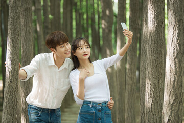 A lovely young couple are having a great time taking pictures using their smartphones in a forested park.