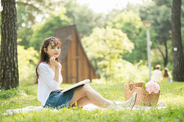 The young woman is having a good time drinking drinks and reading books in a forested park.