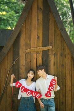 A young couple pose with placards in front of a cabin in the woods.