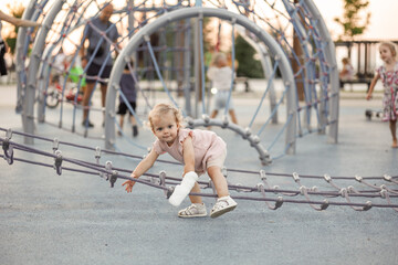 Pretty Toddler girl with a cast on her arm plays on a net, a spider web on the playground. Injury on the playground. Childhood. a two-three-year-old girl, trouble, a broken, an injury, arm in plaster 