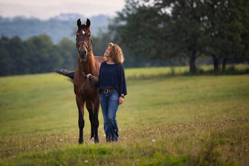 A woman stands with her horse in a meadow and looks up at the horse, smiling.. © RD-Fotografie