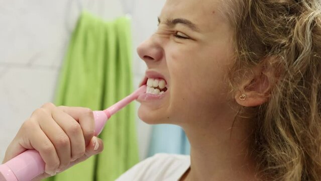 Close-up. A teenage girl brushes her teeth with a modern electric brush. Morning or evening treatments.