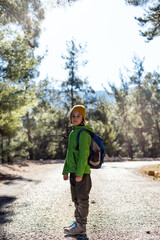 A boy with a backpack in the middle of a forest road, a child is exploring wildlife, a child is standing alone among the trees. Travel and hiking.