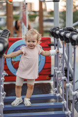 Fototapeta na wymiar Cheerful positive smiling toddler girl walking up a hinged ladder on the playground with a cast on her arm. Trauma during play, kindergarten, active virginity, weekend, white bandage on the arm 