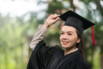 Adult female Asian student in academic gown and graduation hat standing outside college.