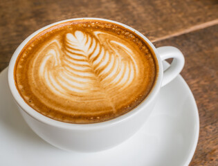 latte art rosetta in a white cup on a wooden table