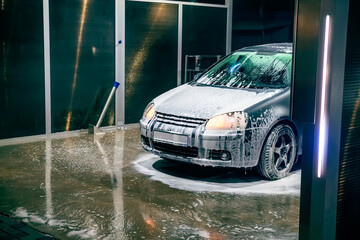A silver, soapy car stands at a self-service car wash.Car wash self-service.