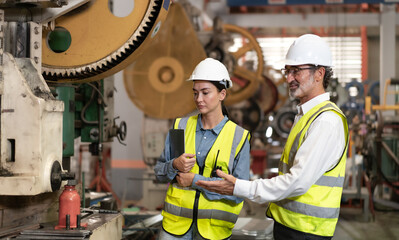 Senior manager on job training female technician working in metal sheet production factory. Skill engineer and team standing in manufacturing facility talking machinery maintenance in heavy mechanic