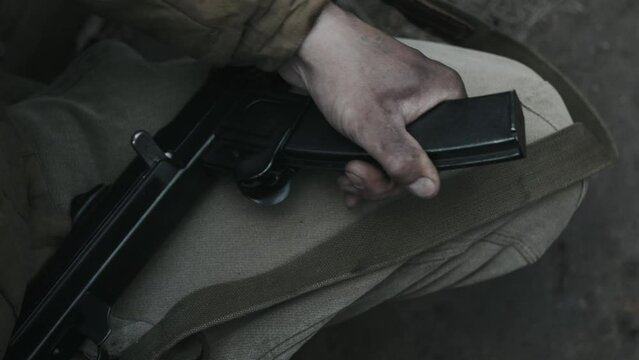 High angle close-up of unrecognizable soldier sitting in frontline trench reloading his rifle