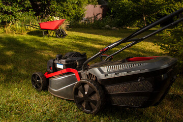 Fototapeta premium Concept of gardening, work, nature. Housework, gardening and country life. Home garden grass cutting woman mowing with lawn mower. Detail of lawn mower. Сutting grass in backyard. Sunny autumn day.