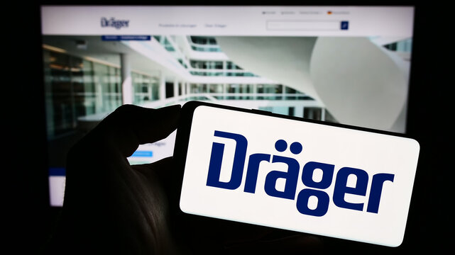 Stuttgart, Germany - 09-09-2023: Person holding mobile phone with logo of German company Dr&auml;gerwerk AG Co. KGaA (Dr&auml;ger) on screen in front of web page. Focus on phone display.
