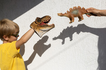 boy and mom are playing with toy dinosaur, creating interesting contrasting shadows from it on...
