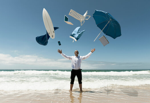 A Man Stands In The Ocean With Items From Work And Vacation Flying Over His Head; Tarifa, Cadiz, Andalusia, Spain