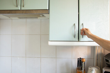 Woman's hand opens kitchen cabinet under sunlight, kitchen furniture