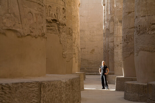 A Woman Tourist Stands At The Base Of The Massive Columns In The Temples Of Karnak On The East Bank Of Luxor Along The Nile River; Egypt