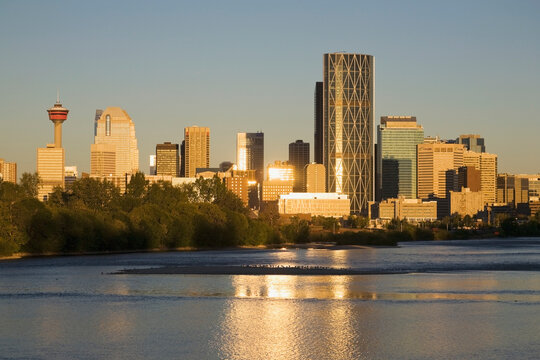 Calgary cityscape along river with reflections on building and river at sunrise with blue sky; Calgary alberta canada