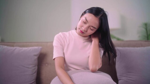 An Asian woman do self massage at her neck and sitting in the wrong position on the sofa at home, People with body-muscles problem and health care concept.