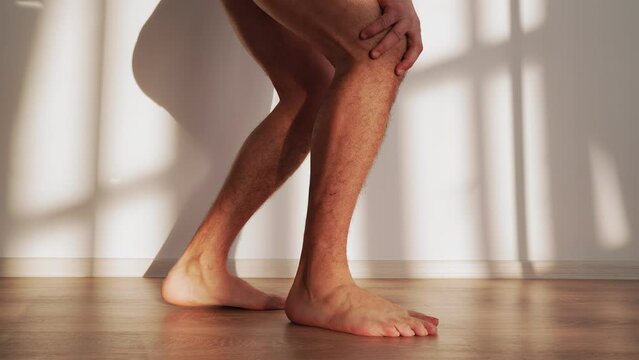 Unrecognizable Man Walks Through the House and Clutches His Knee in Pain. Concept of Joint Diseases and Injuries. Slow Motion.